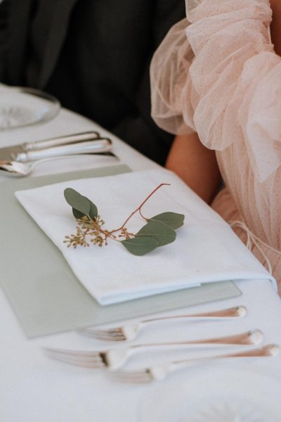 A closeup shot of a female wearing a dress sitting in front of a wedding table with a napkin and green leaf on it
